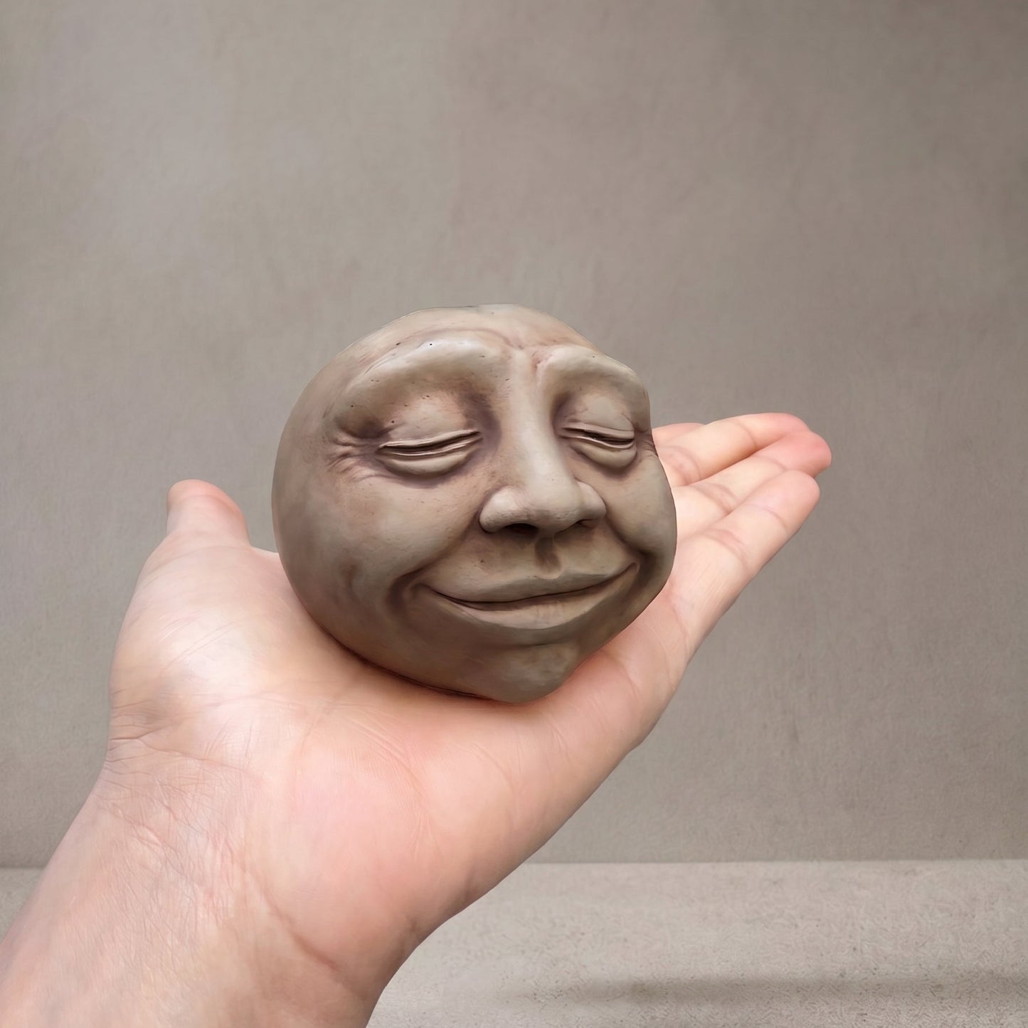  Concrete head sculpture resting in an open palm to show its size, with the word Sing pressed into the back Glow_ Stone 