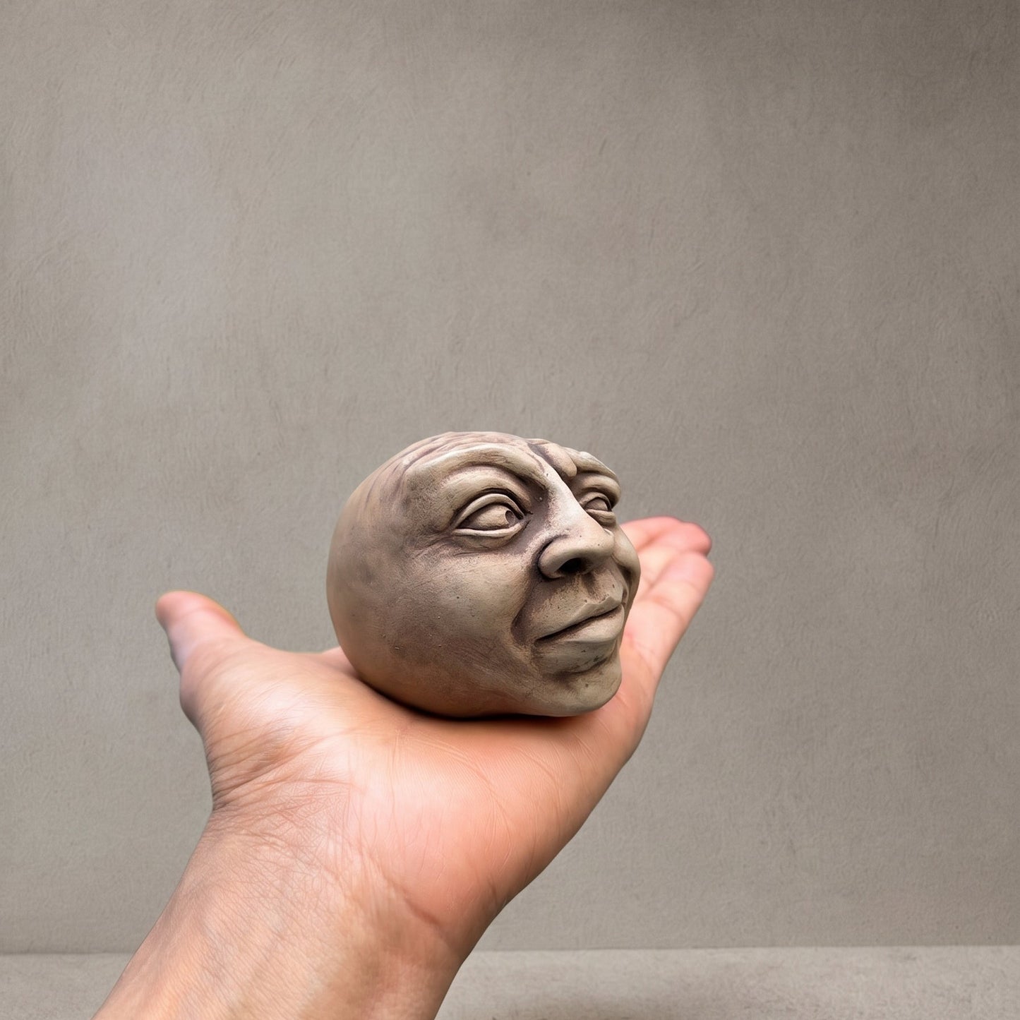 Concrete head sculpture resting in an open palm to show its size, with the word Scrunch Stone pressed into the back