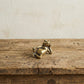 The Content Spirit miniature brass frog held in hand to show scale, with relaxed reclining pose and golden patina