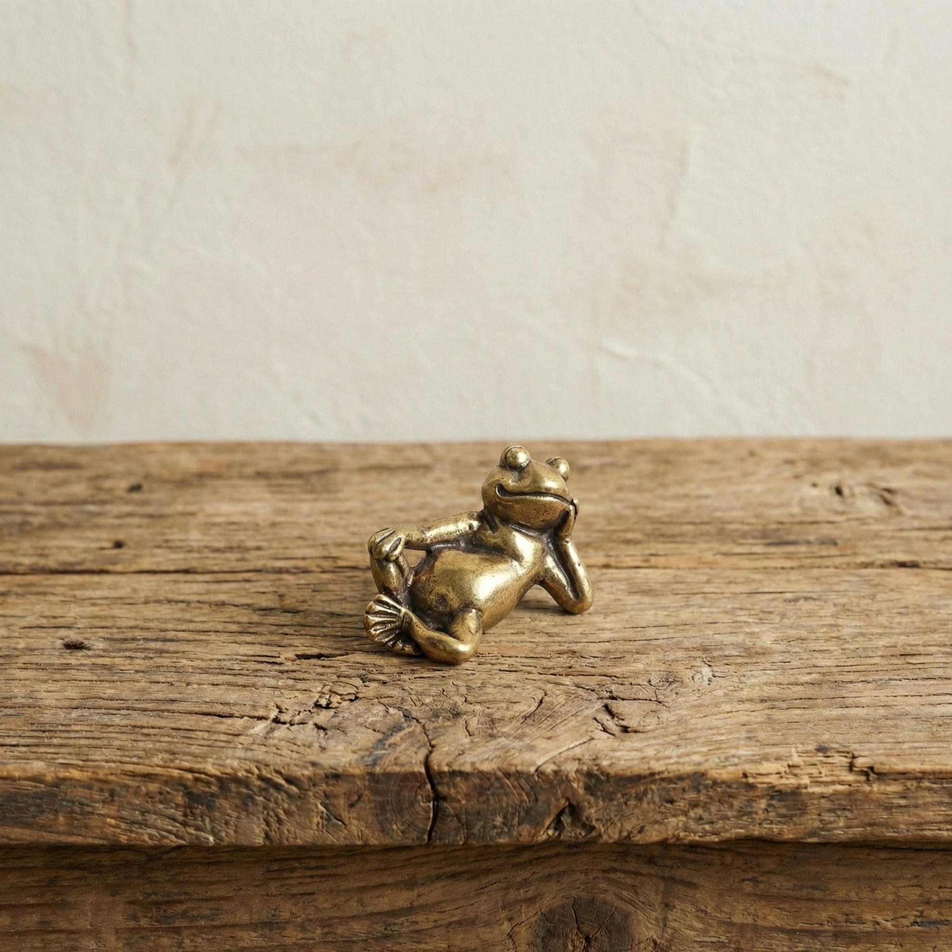The Content Spirit miniature brass frog held in hand to show scale, with relaxed reclining pose and golden patina