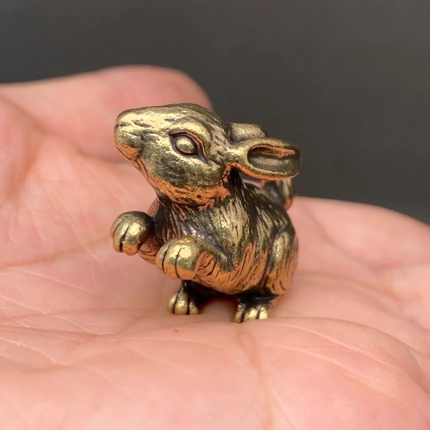The Curious Sentinel miniature brass standing bunny held in hand to show scale, with detailed fur texture and golden patina