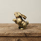 The Curious Sentinel miniature brass standing bunny on a wooden surface, upright on hind legs with ears raised and warm aged patina, from the WILLAGE Tiny Objects collection