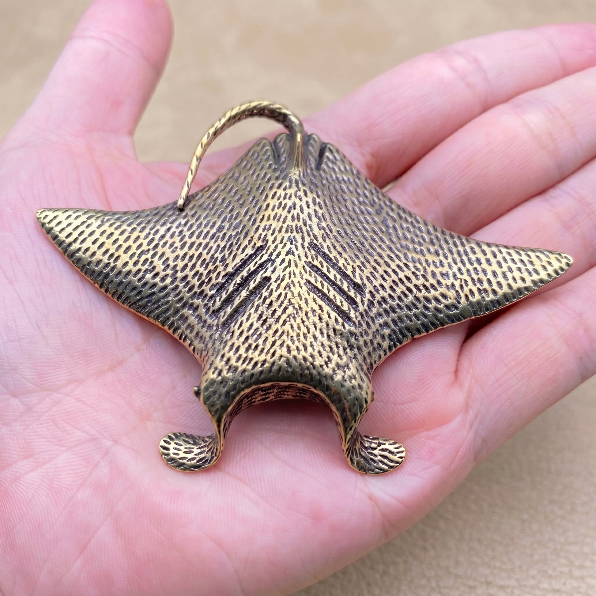The Drifter brass manta ray held in a hand to show its size, about 3.3 inches across