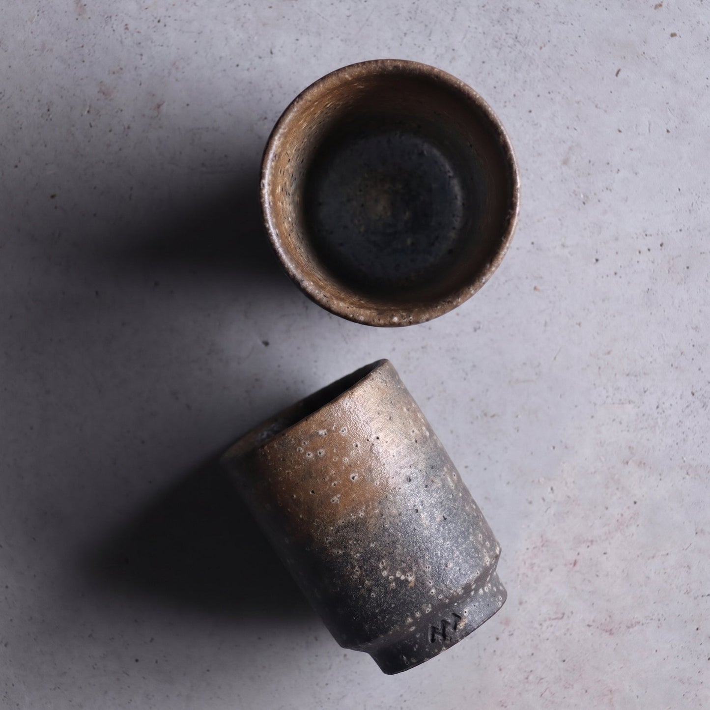 Tall unglazed Iga ware stoneware cup in dark charcoal with bronze shimmer and a pebbled surface, on a white background