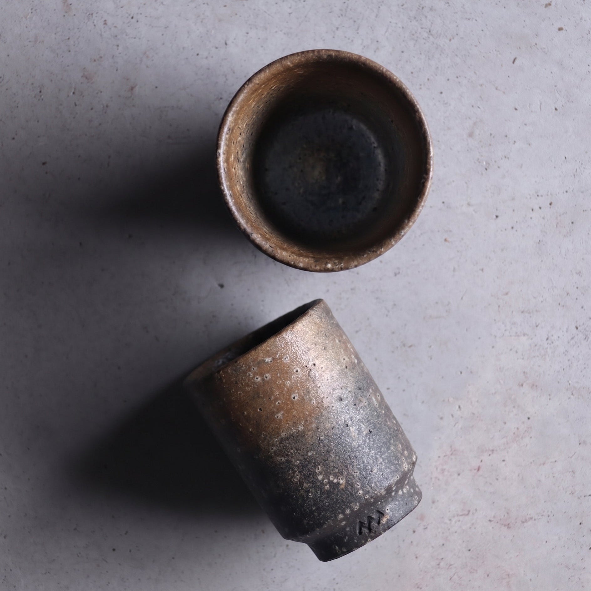 Tall unglazed Iga ware stoneware cup in dark charcoal with bronze shimmer and a pebbled surface, on a white background