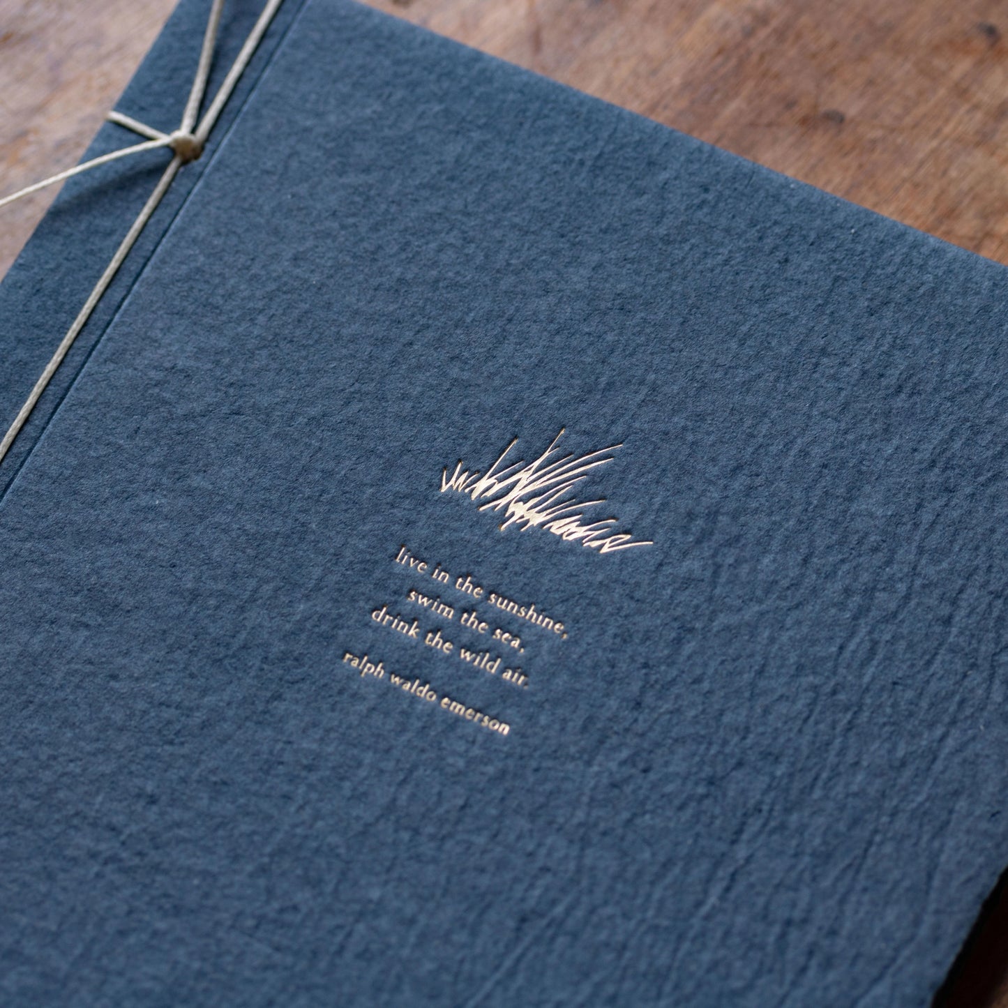 Close-up of champagne foil letterpress grass motif and Emerson quote on denim blue handmade paper journal cover