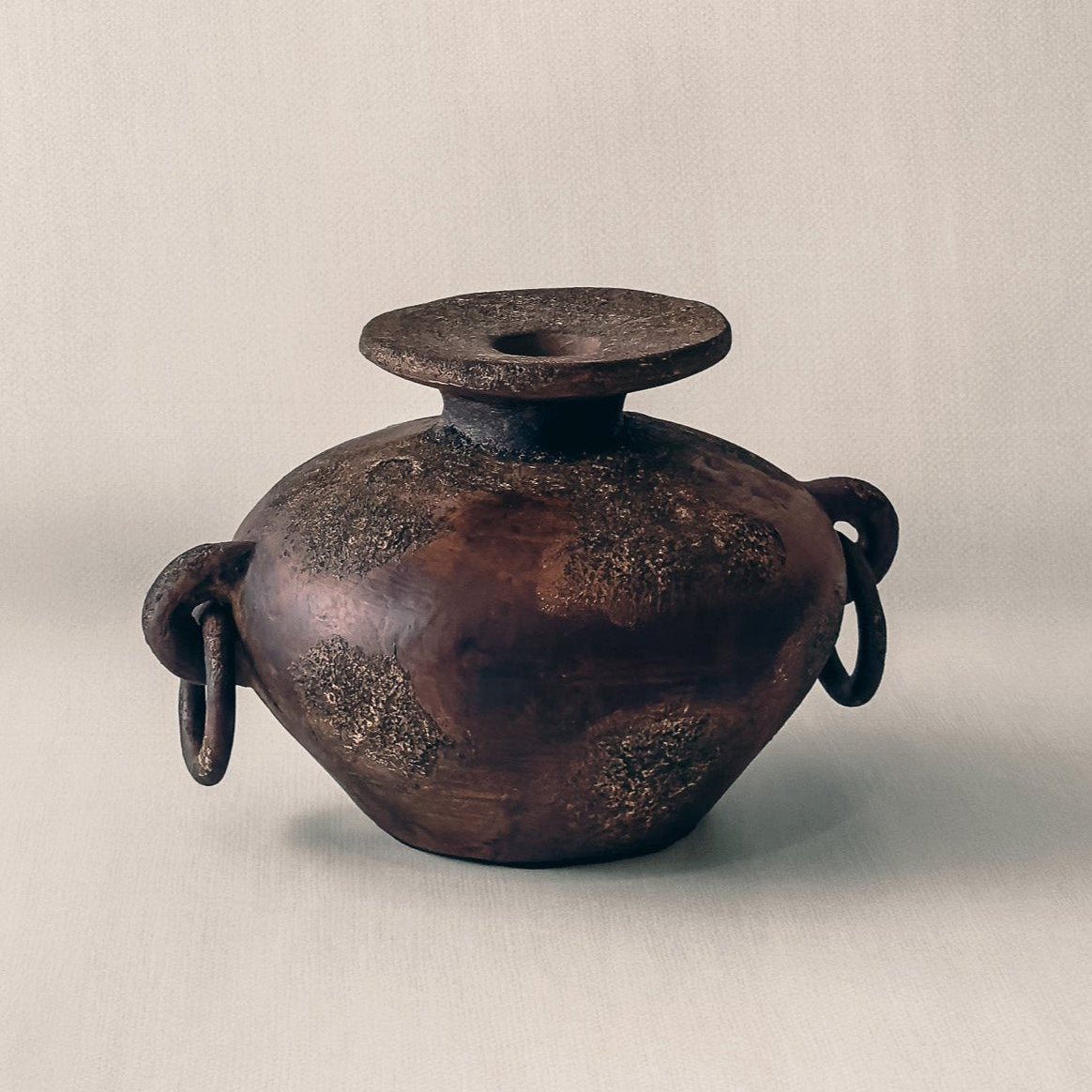Febi terracotta vessel shown from angle, showing iron ring handles and aged brown finish, from Indonesia