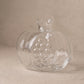 Two clear glass pomegranate vases, large and small, on a dark wooden tray holding a pink flower and green sprigs