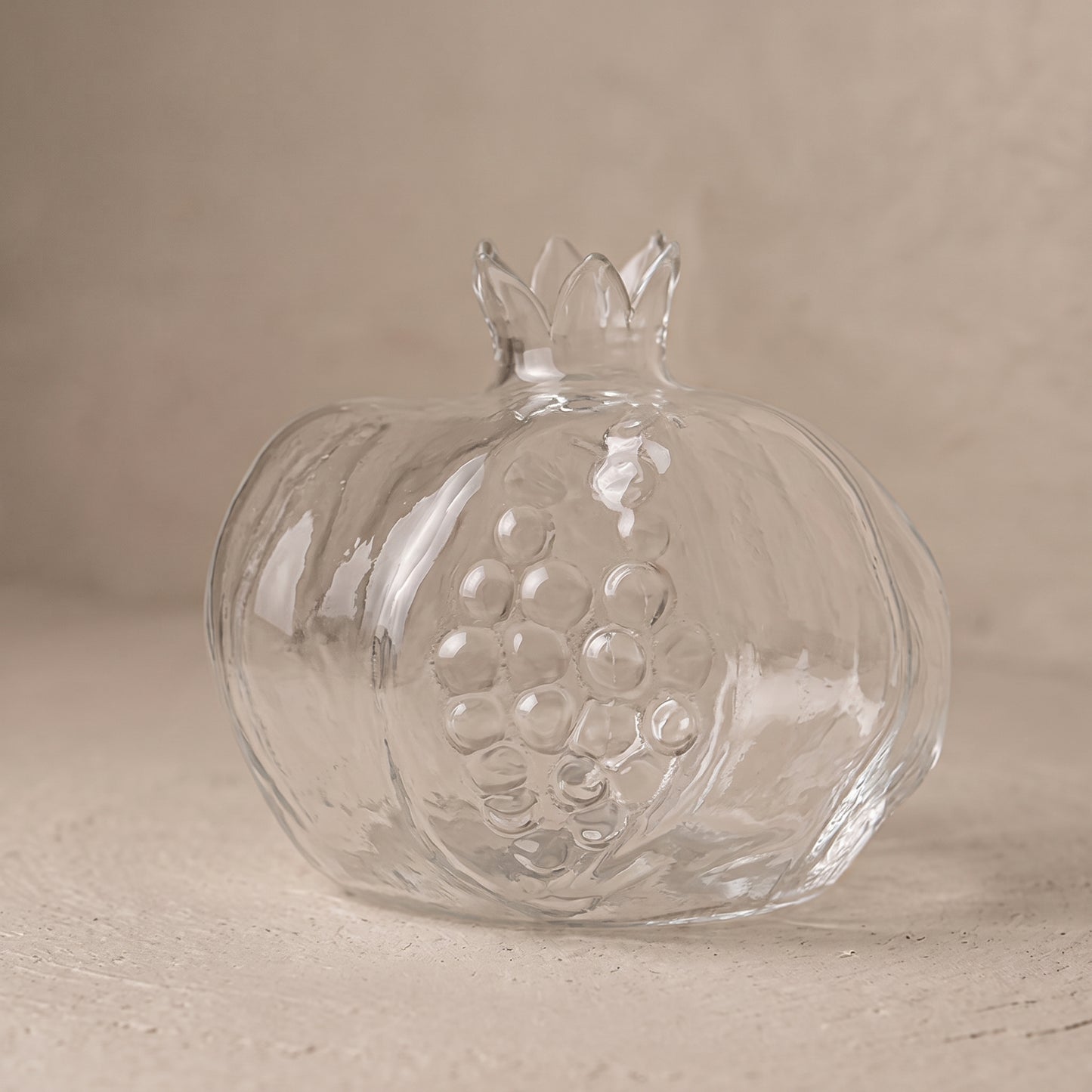Two clear glass pomegranate vases, large and small, on a dark wooden tray holding a pink flower and green sprigs