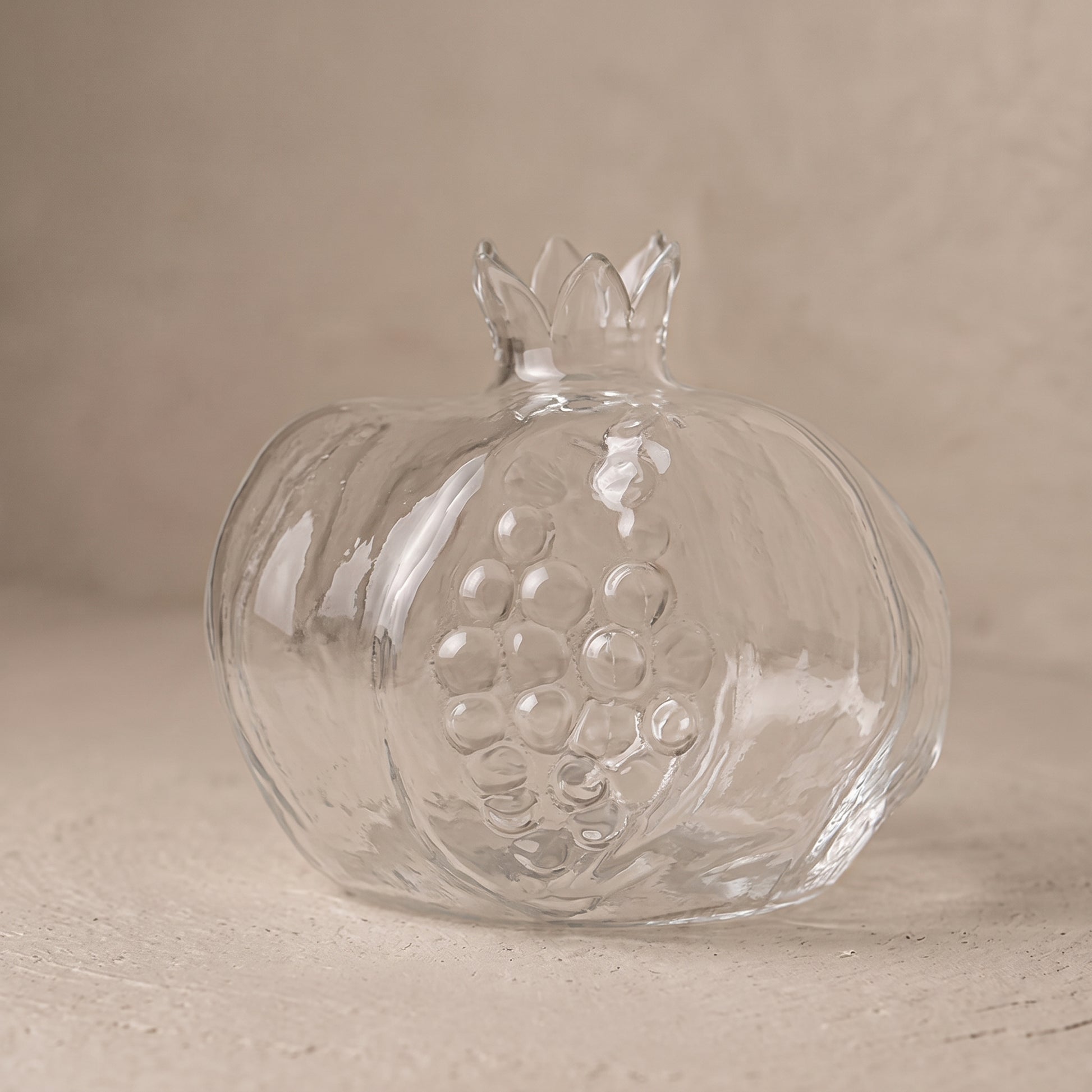 Two clear glass pomegranate vases, large and small, on a dark wooden tray holding a pink flower and green sprigs