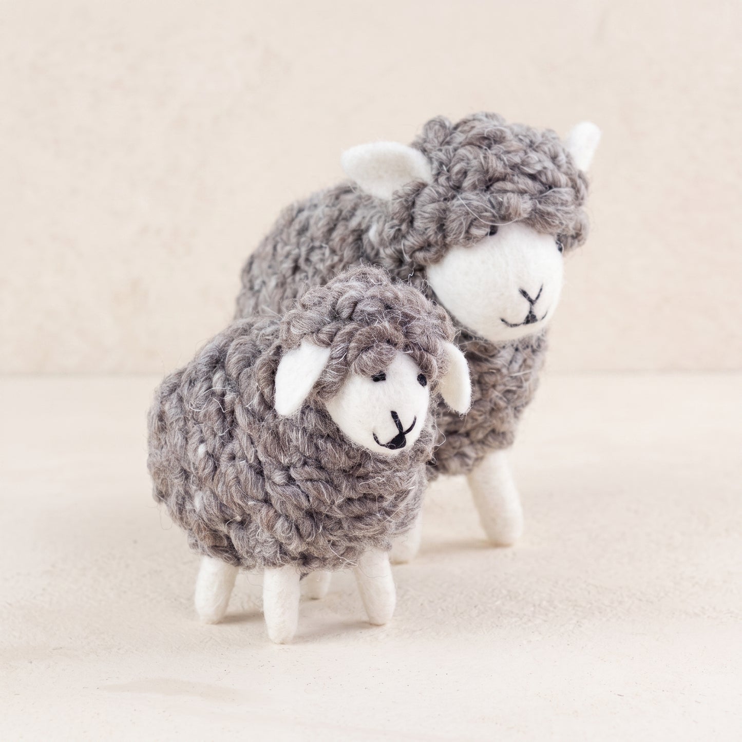 Two wooly hand-felted sheep in natural grey wool with cream faces and legs, large and small, on a white background