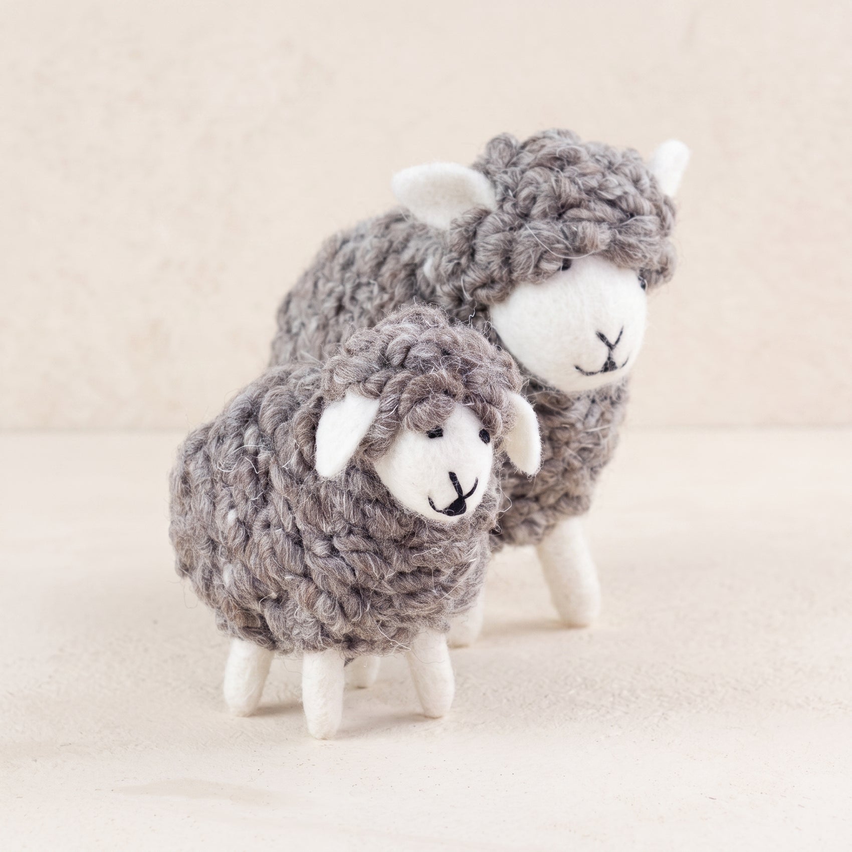 Two wooly hand-felted sheep in natural grey wool with cream faces and legs, large and small, on a white background