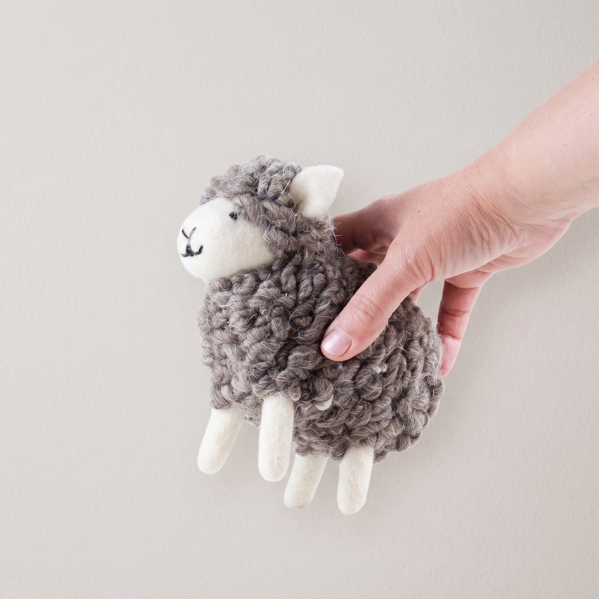 Large wooly felted grey sheep held in a hand to show its size and looped wool fleece