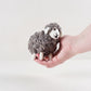 Small wooly felted grey sheep resting in an open hand, showing its stitched face and floppy ears