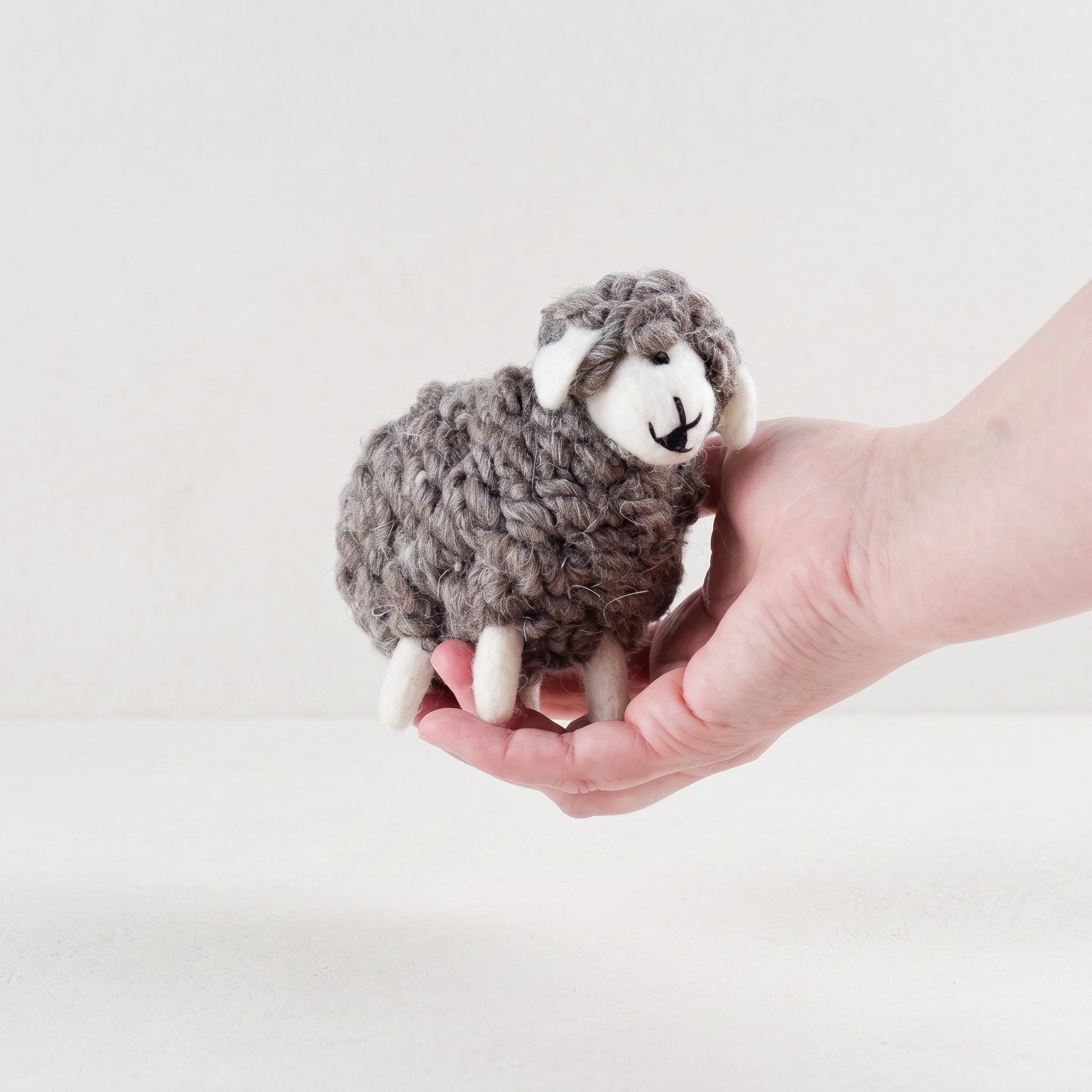 Small wooly felted grey sheep resting in an open hand, showing its stitched face and floppy ears