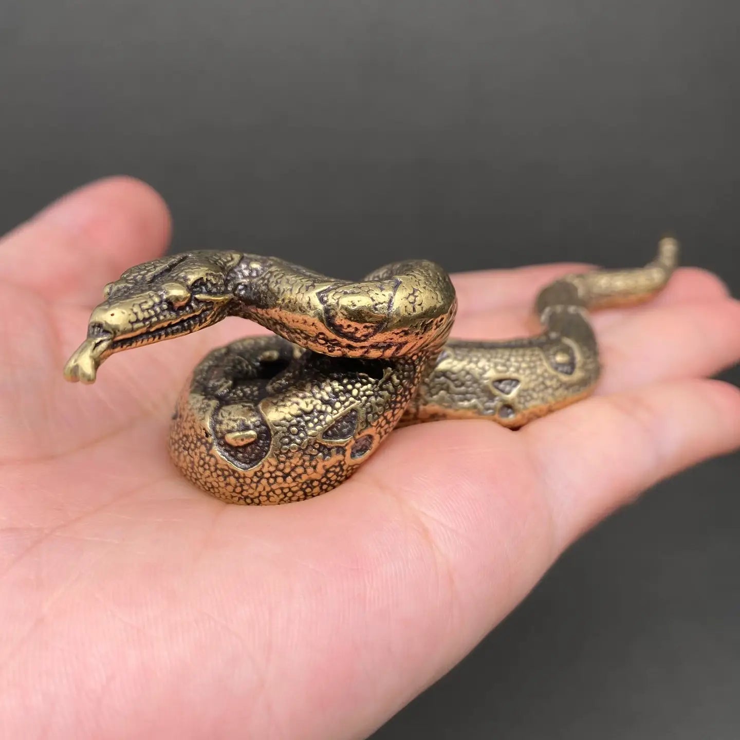 The Fluid Guardian miniature brass python held in hand to show scale, with raised head and golden patina
