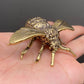 Brass bee figurine held in an open palm to show its palm-sized scale, veined wings, and textured thorax
