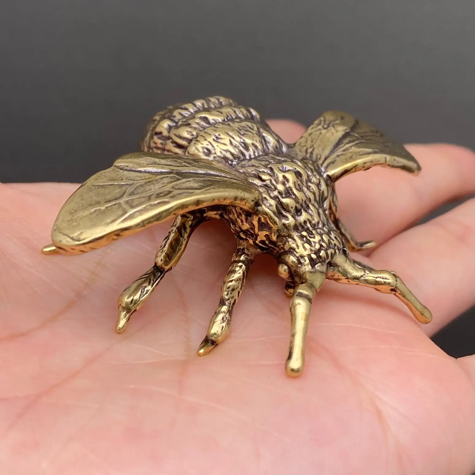 Brass bee figurine held in an open palm to show its palm-sized scale, veined wings, and textured thorax