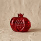 Deep red glass pomegranate bud vase with an open crown top, photographed on a white background