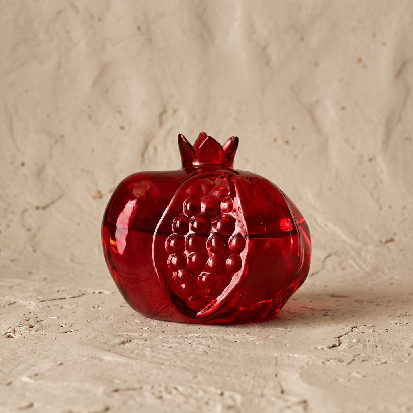 Deep red glass pomegranate bud vase with an open crown top, photographed on a white background