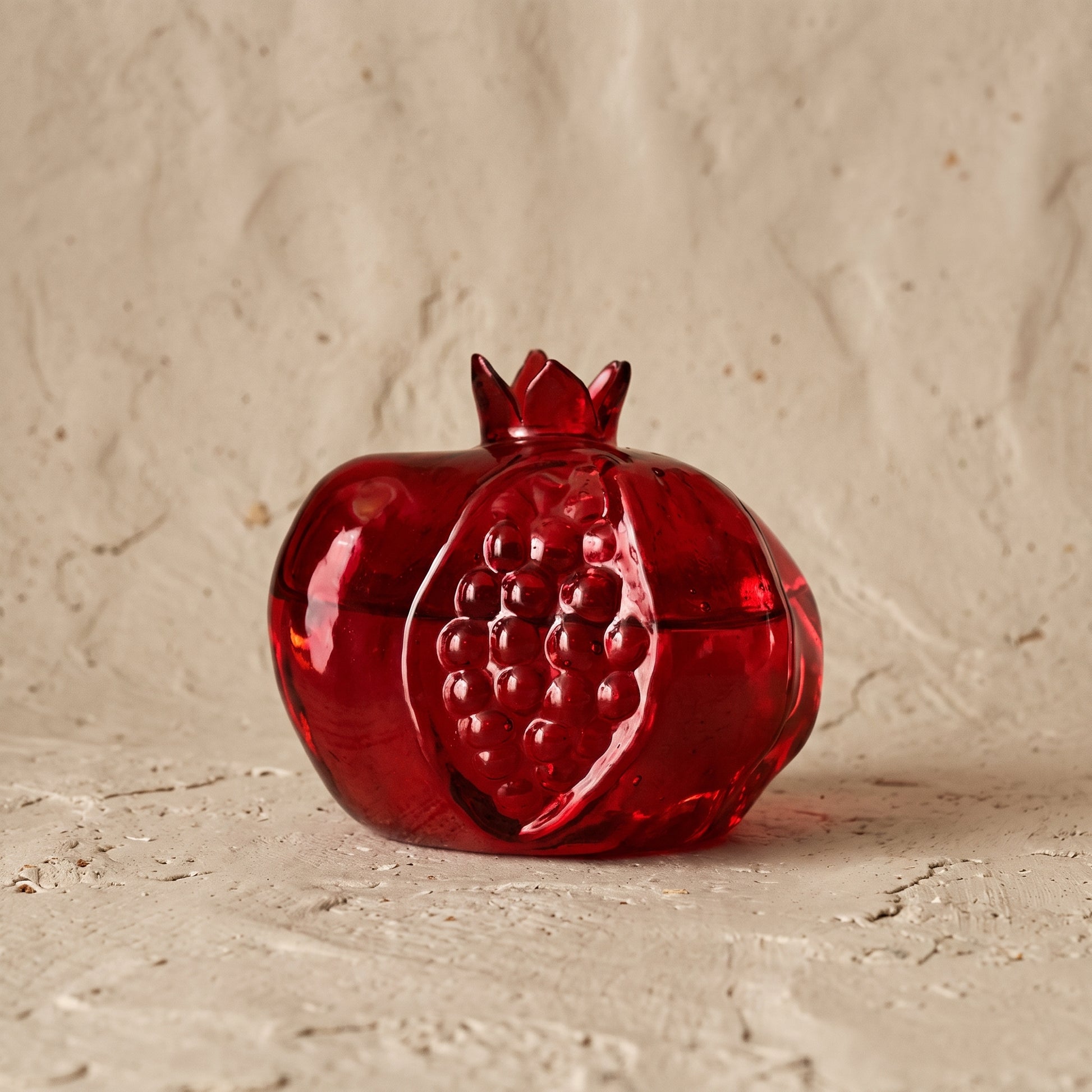 Deep red glass pomegranate bud vase with an open crown top, photographed on a white background