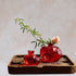Large and small red glass pomegranate vases on a wooden tray, one holding a flowering stem