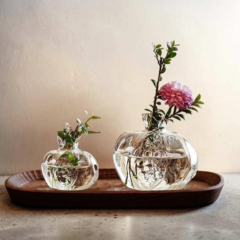 Clear glass pomegranate bud vase with a crown-shaped opening and pressed seed detail, on a white background