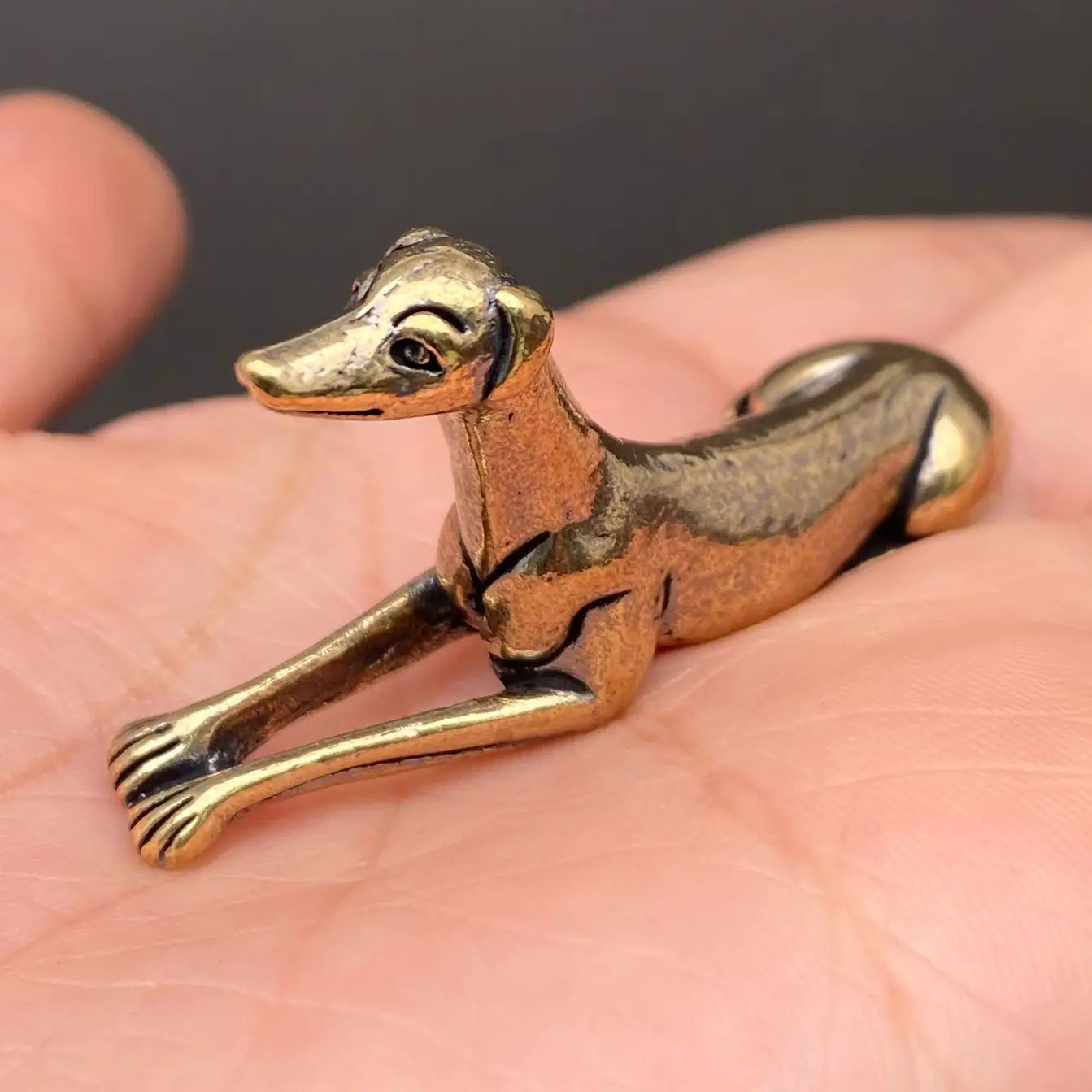 The Graceful Sentinel miniature brass greyhound in a reclining pose with elegant proportions and warm aged patina on a wooden surface, from the WILLAGE Tiny Objects collection
