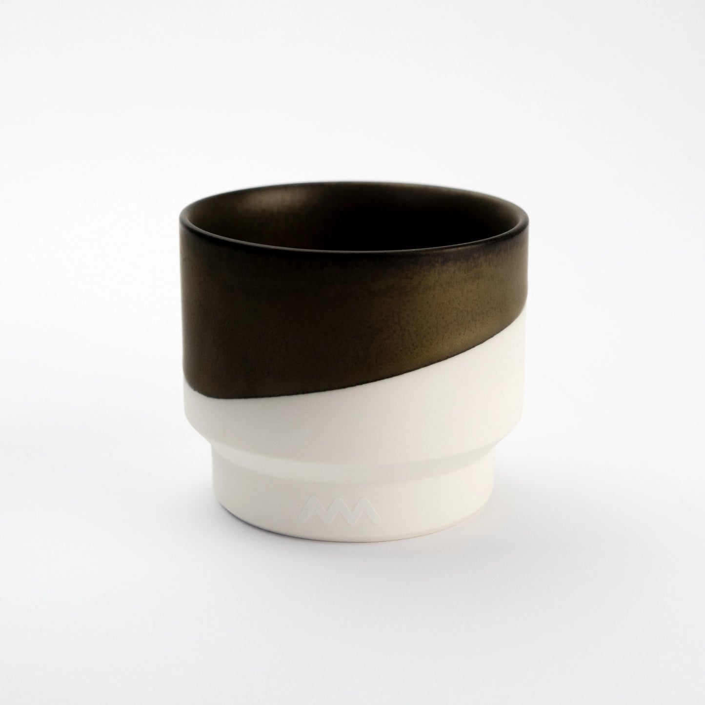 Porcelain cup half-dipped in dark bronze glaze over a raw white porcelain base, photographed on a pale gray background