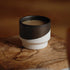 dipped porcelain cup holding a hot drink, resting on an olive-wood board in warm light