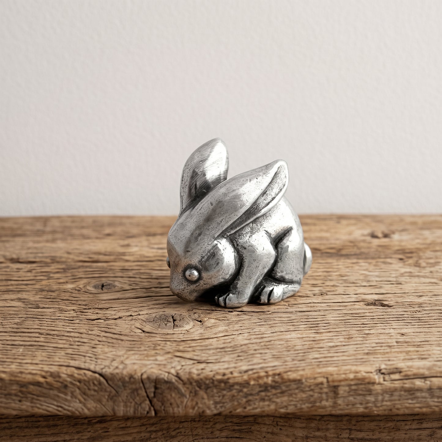 Small pewter rabbit netsuke with ears laid back, sitting on botanical-print paper