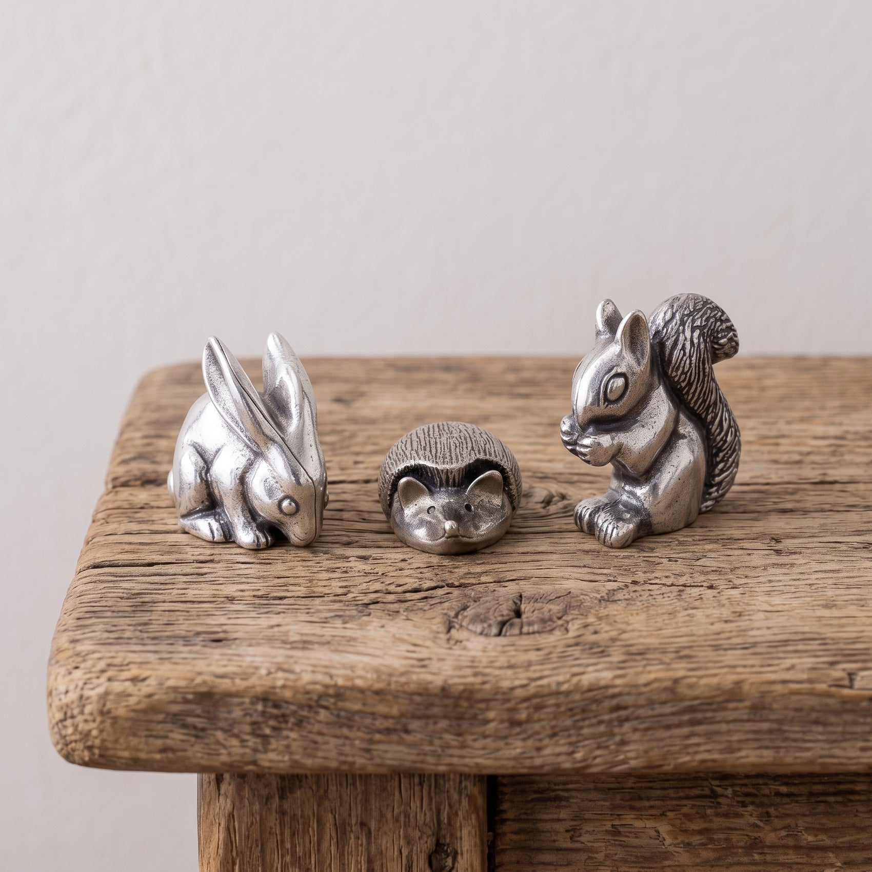 Set of three pewter netsuke figurines — a rabbit, a curled hedgehog, and a squirrel — photographed together on a gray background
