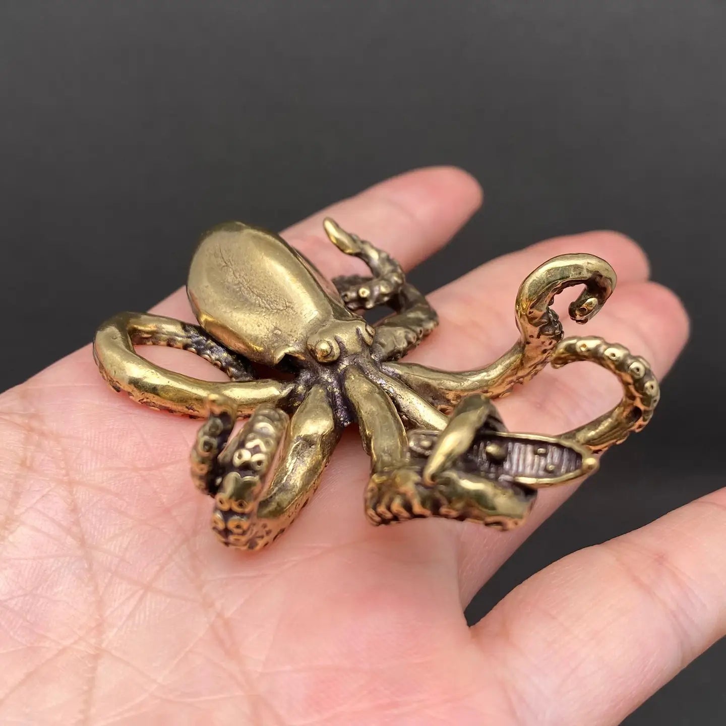  Brass octopus figurine held in an open hand to show its palm-sized scale, tentacles curling around a small brass boat