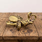 Solid brass octopus figurine with curling tentacles cradling a small boat, antique patina finish, shown on a clear stand against a gray background