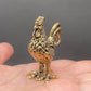 The Herald brass rooster held in a hand to show its small size, about 2 inches tall