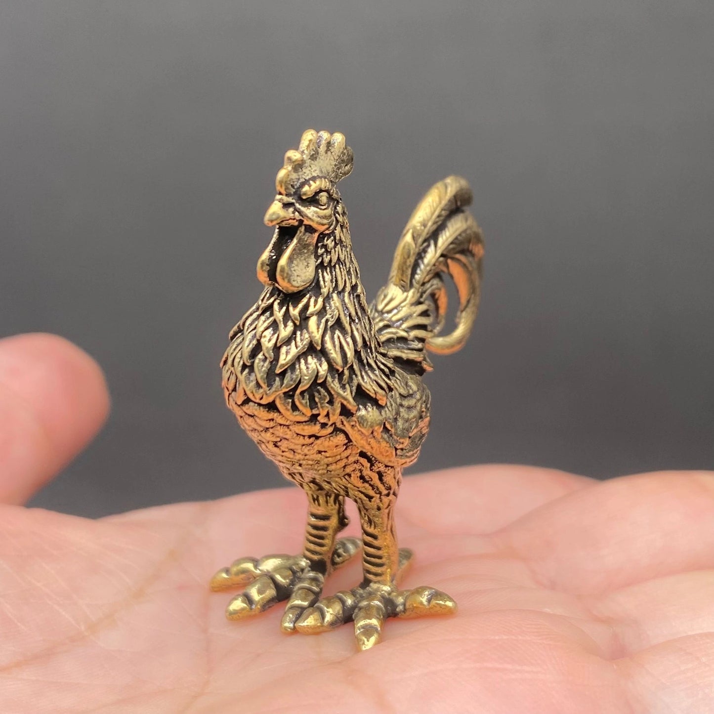 The Herald brass rooster held in a hand to show its small size, about 2 inches tall