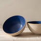 Two handmade stoneware bowls in large and small sizes, each with a deep blue glazed interior and a natural unglazed exterior