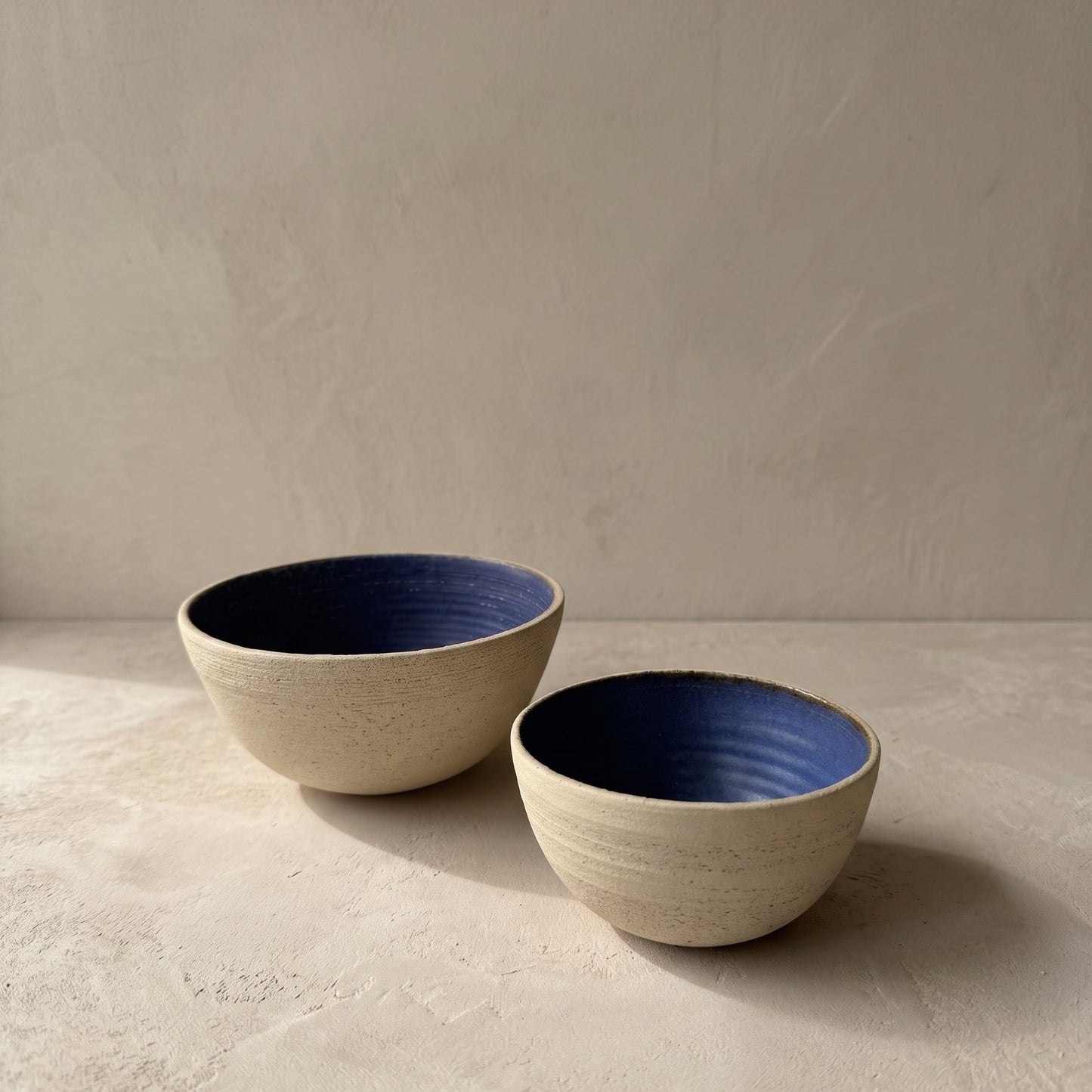 Two stoneware bowls, one tilted to show the blue glazed interior with visible potter's wheel rings