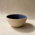 A handmade stoneware bowl with a deep blue glazed interior and a sand-textured unglazed exterior, lit from the side
