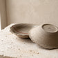 Handmade stoneware plate turned over to show the unglazed base, raw clay texture and the maker's stamp, beside a second plate with its red line visible