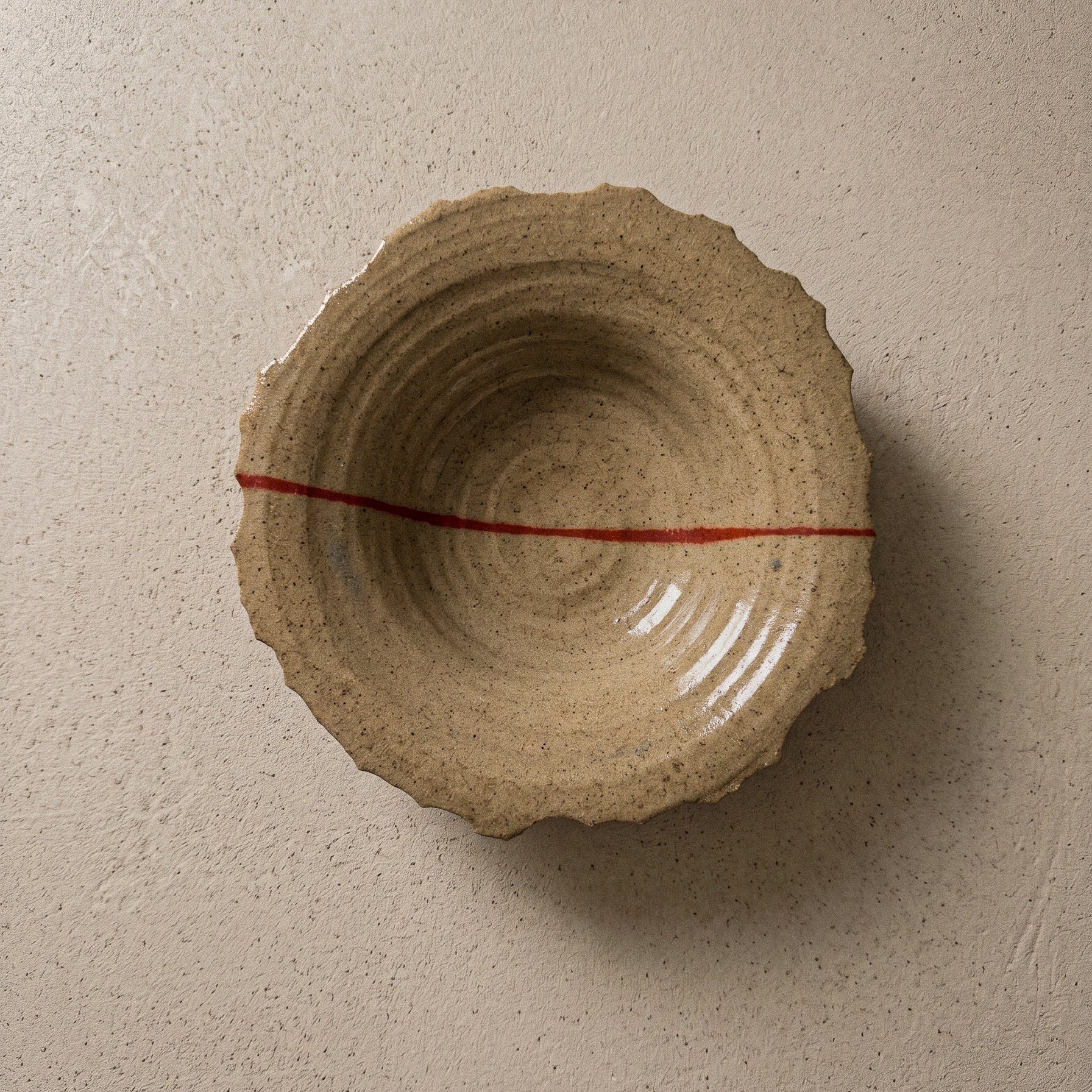 Handmade stoneware plate seen from above, sandy speckled clay with a torn organic edge, ridged wheel-thrown interior and a single red line running across it