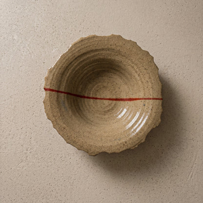 Handmade stoneware plate seen from above, sandy speckled clay with a torn organic edge, ridged wheel-thrown interior and a single red line running across it