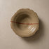 Handmade stoneware plate seen from above, sandy speckled clay with a torn organic edge, ridged wheel-thrown interior and a single red line running across it