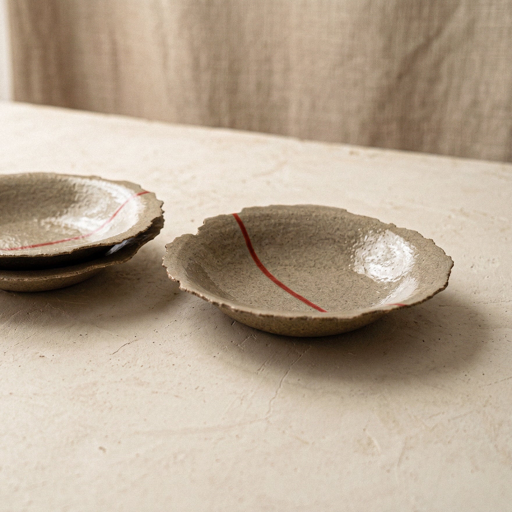 Two handmade stoneware plates on a pale surface, one angled to show the shallow curve, torn rim and glazed interior