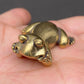The Jovial Companion miniature brass frog held in hand to show scale, with playful reclining pose and golden patina