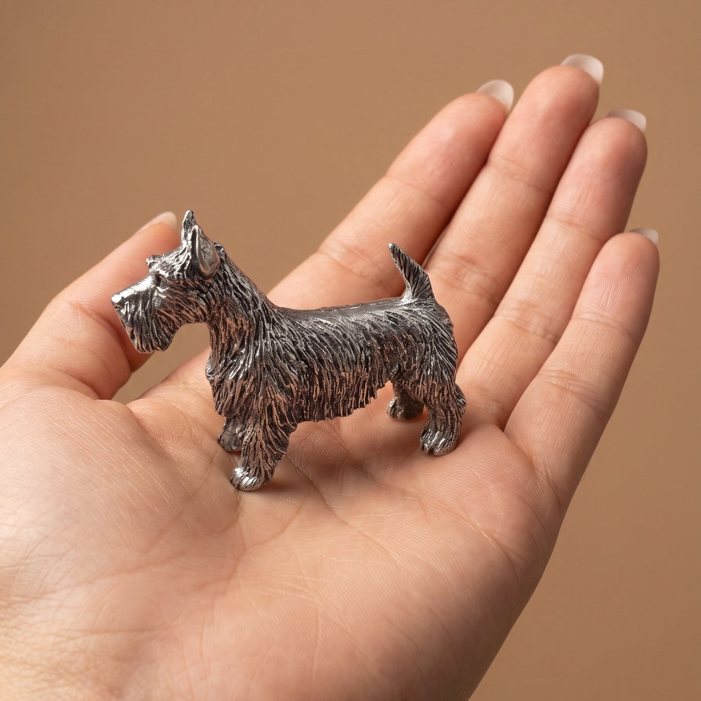 Pewter Scottish Terrier figurine standing in an open palm, showing its palm-sized scale and detailed wiry coat