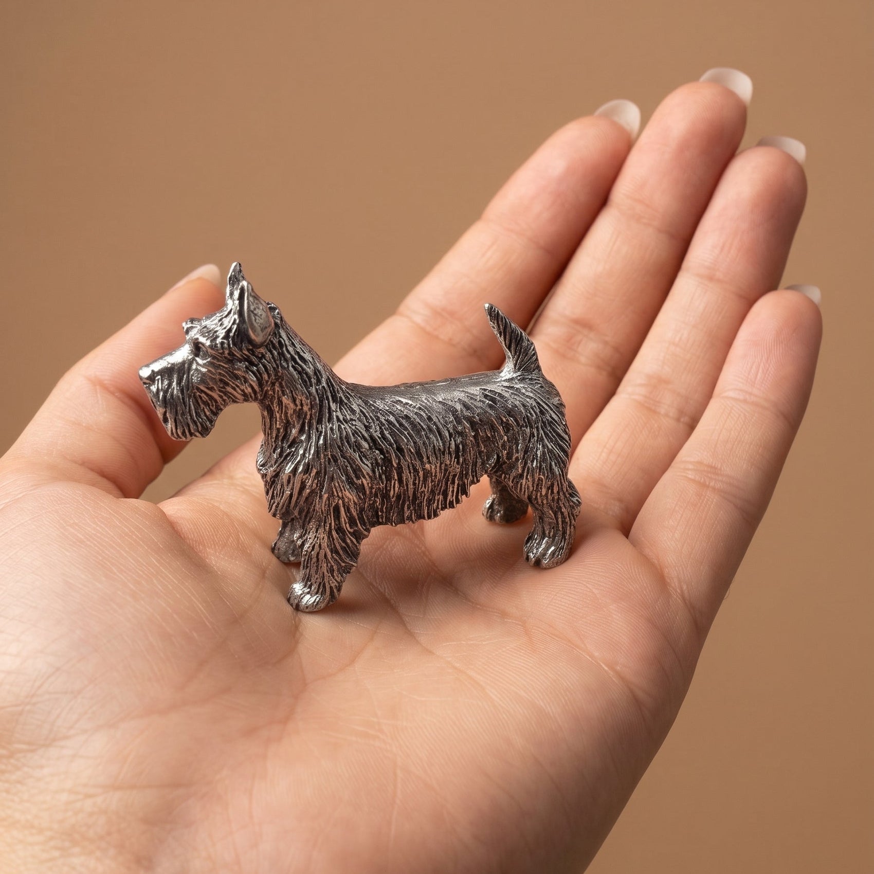 Pewter Scottish Terrier figurine standing in an open palm, showing its palm-sized scale and detailed wiry coat