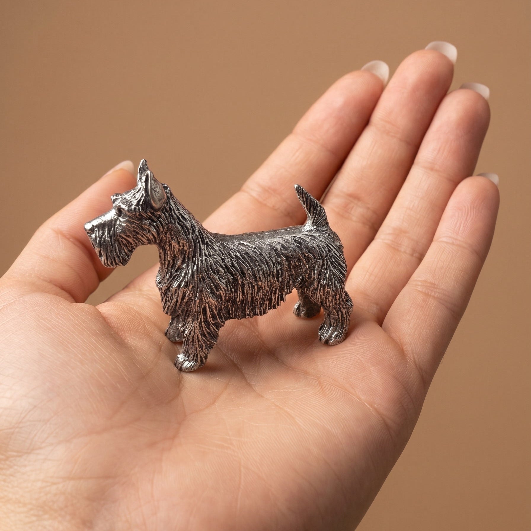 Pewter Scottish Terrier figurine standing in an open palm, showing its palm-sized scale and detailed wiry coat