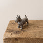 Small pewter Scottish Terrier figurine with pricked ears and raised tail, standing on a rustic wooden shelf