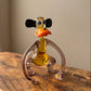 Front view of The Lanky Ape lampworked glass monkey figurine showing face detail with blue eyes, orange lips, and black floppy ears, amber solid glass by Glass by Iness